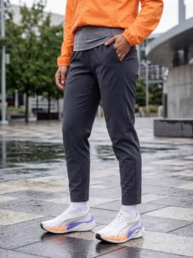 Velocity Nitro 4 Goretex Womens – A rainy-day outdoor ensemble with water-resistant charcoal joggers, a bright orange technical windbreaker to match the shoe's accents, and a reflective headband.