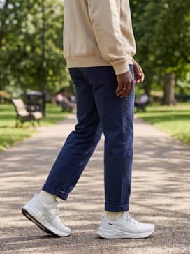 Navy blue straight-leg chinos cuffed at the ankle to show off the shoe silhouette, paired with a beige oversized graphic sweatshirt for a modern streetwear aesthetic.