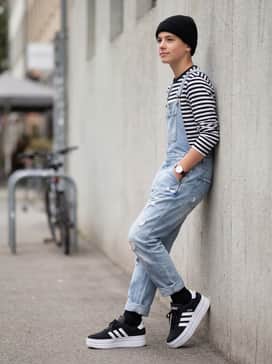 Distressed denim overalls worn over a striped long-sleeve tee, finished with a black beanie for a playful yet edgy weekend outfit.