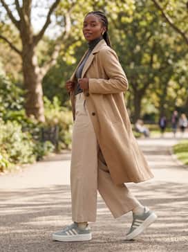 Wide-leg beige trousers, a fitted charcoal turtleneck, and a long tan trench coat.