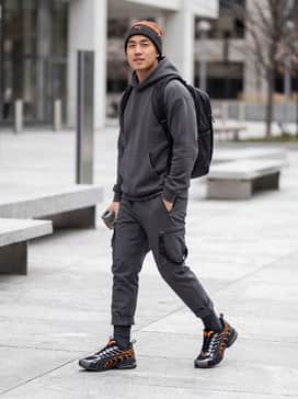 Voltra Mens Sneakers – A technical streetwear ensemble featuring black tapered cargo joggers with utility straps, a charcoal tech-fleece hoodie, and an orange-accented beanie to mirror the shoe's vibrant highlights.