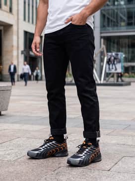 A modern casual look with distressed slim-fit black jeans, an oversized white graphic tee featuring orange typography, and a grey nylon bomber jacket.