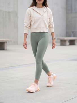 A sleek pair of high-waisted sage green athletic leggings paired with a cropped cream-colored zip-up hoodie and white no-show socks.