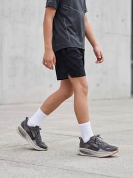 A performance-focused look featuring black moisture-wicking shorts, a grey technical tee with reflective details, and white crew socks to highlight the dark grey upper.