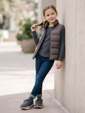 A casual weekend ensemble with slim-fit dark indigo jeans, a charcoal grey long-sleeve thermal, and a lightweight puffer vest in a neutral earth tone.