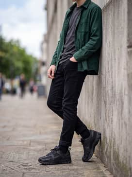 A modern streetwear outfit pairing slim-fit tapered black denim with a bold graphic t-shirt and an unbuttoned flannel shirt in forest green.