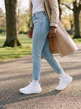 Vomero Plus – A sporty urban style using light-wash slim-fit denim jeans cuffed at the ankle, a tucked-in white graphic tee, and a beige trench coat for a sophisticated mix of textures.
