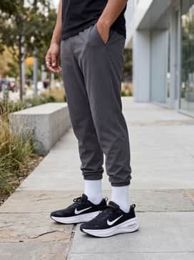 Tapered charcoal grey joggers, a black oversized graphic t-shirt, and a sleek nylon bomber jacket for a modern streetwear aesthetic.