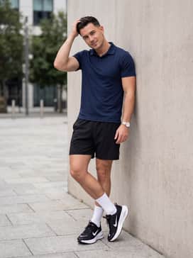 Black technical athletic shorts worn with a fitted moisture-wicking polo in navy blue and classic white crew socks for a sporty summer ensemble.