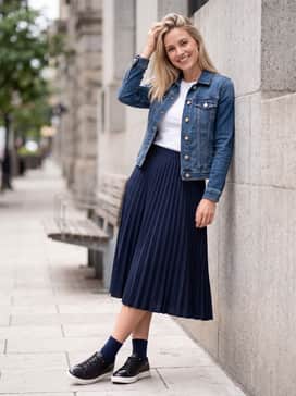 A navy blue midi-length pleated skirt combined with a fitted white tee and a denim jacket for a feminine yet relaxed weekend outfit.