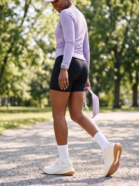 Womens Grandpr Allday Running Shoes – Black bike shorts, a lavender moisture-wicking long-sleeve top, and a white baseball cap for an athletic, outdoor-ready ensemble.