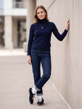 Dark wash straight-leg jeans with a slight cuff, worn with a fitted navy turtleneck and delicate gold jewelry to complement the shoe's branding.