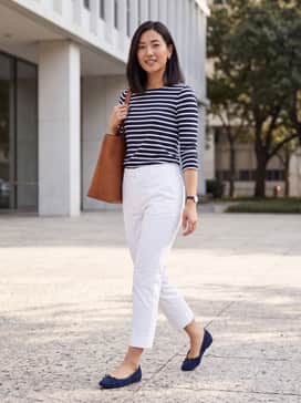 A navy blue and white striped Breton top paired with cropped white trousers and a tan leather tote bag for a nautical-inspired look.