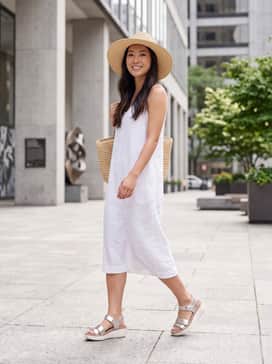 A breezy white linen midi dress paired with a straw sun hat and a woven tote for a timeless coastal look.