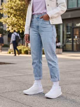 Light-wash high-rise mom jeans with the hems cuffed, a tucked-in pastel graphic tee, and a white denim jacket for a bright weekend look.