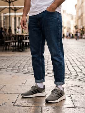 Dark wash tapered denim jeans with a slight cuff, a crisp white crewneck sweatshirt, and a charcoal baseball cap for a clean weekend outfit.