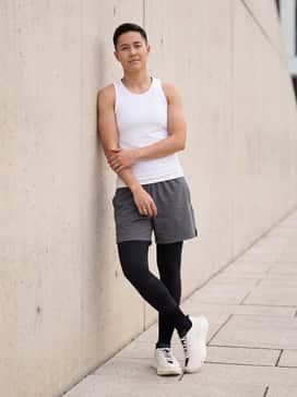 A high-performance running outfit with black moisture-wicking compression tights, graphite grey athletic shorts, and a sleek white seamless tank top.