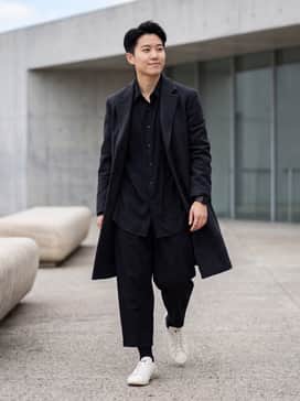 An all-black Yohji Yamamoto-inspired look featuring oversized cropped trousers, a draped black button-down shirt, and a structured charcoal overcoat.