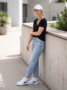 A relaxed weekend ensemble consisting of light-wash distressed boyfriend jeans, a tucked-in black graphic tee, and a matching white baseball cap.