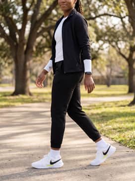 A modern street-style outfit with sleek black joggers, a fitted white long-sleeve crop top, and a black puffer vest for layering in cooler weather.