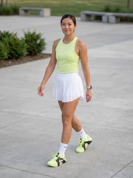 Zoom Gp Challenge 15 Prm – A professional court-ready look featuring a crisp white pleated tennis skirt, a lime green moisture-wicking racerback tank top, and white performance crew socks.