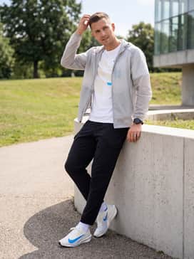 An urban streetwear ensemble with black nylon cargo pants, a white graphic t-shirt with blue lettering, and a translucent windbreaker jacket.