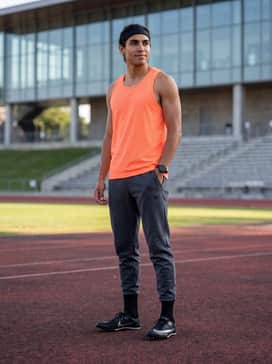 A neon-colored mesh tank top for visibility during training, worn with charcoal grey tech-fleece leggings and a lightweight headband.