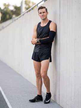 A team-branded athletic singlet coordinated with split running shorts and a matching sweat-wicking arm sleeve for a professional race-day look.