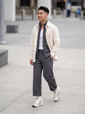 A pair of wide-leg charcoal grey trousers, a fitted white ribbed tank top, and an oversized vintage leather racing jacket for a high-low streetwear aesthetic.