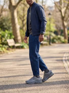 Zoom Vomero Roam – Dark indigo tapered jeans, a grey graphic sweatshirt, and a navy blue bomber jacket for a classic, everyday streetwear outfit.